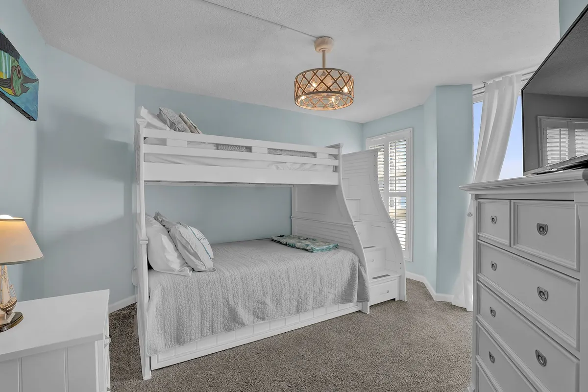 A playful second bedroom with a sturdy bunk bed, decorative lamp, dresser, and cheerful artwork on the wall. The space is inviting for children or extra guests, offering a cozy yet fun sleeping area.