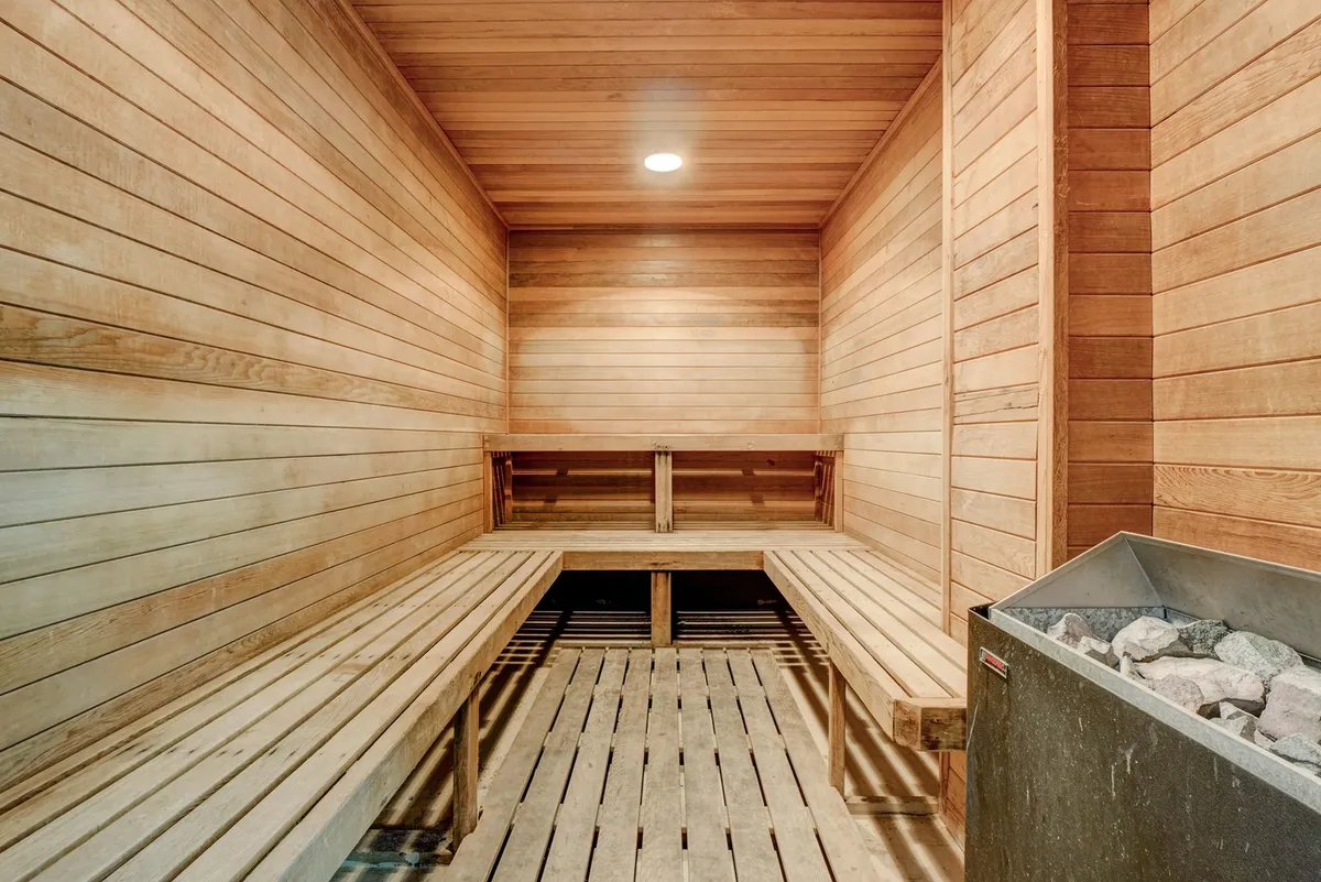 A tranquil sauna with classic wooden benches and a stone heater, enveloped in warm wood paneling. The space offers a serene retreat for relaxation and post-workout recovery.