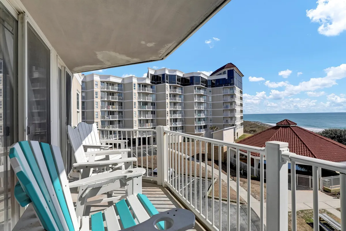 A serene balcony scene featuring comfortable chairs and a direct view of the ocean. The architecture of the building is visible, with a relaxing outdoor atmosphere perfect for working, unwinding, or enjoying coffee breaks while soaking in the coastal scenery.