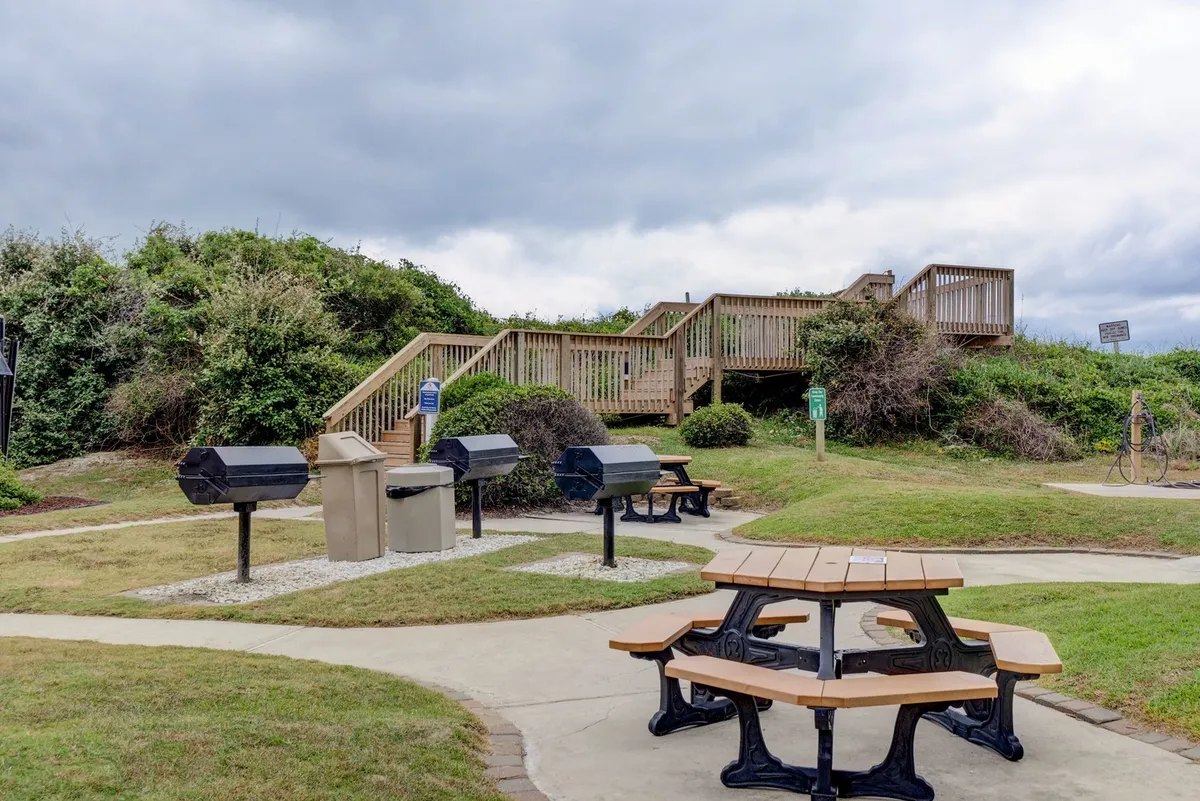 A relaxed outdoor area with picnic tables and barbecue grills surrounded by greenery. Families and friends gather for casual meals, laughter, and community events, set against a backdrop of nature trails and resort landscaping.