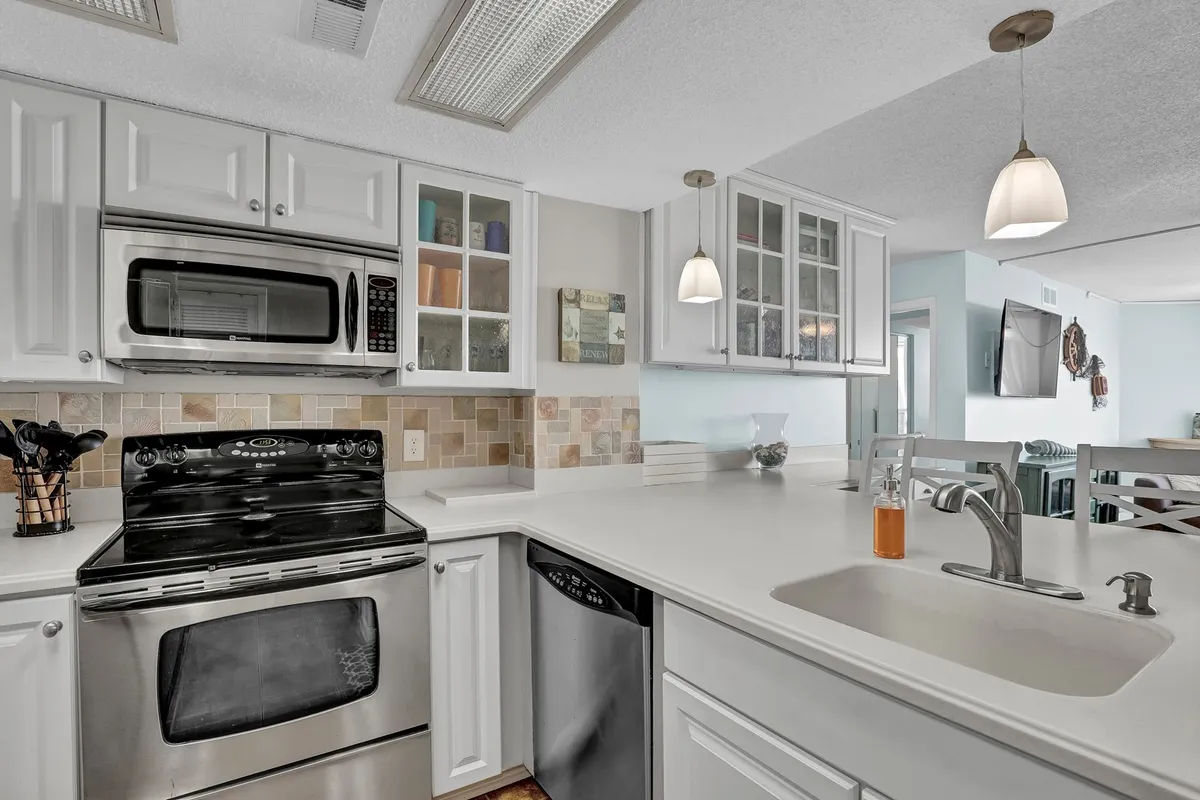 A cheerful, contemporary kitchen featuring stainless steel appliances, white cabinetry, ample countertop space, and a central kitchen island. The scene is well lit and laid out for both cooking and family gatherings.