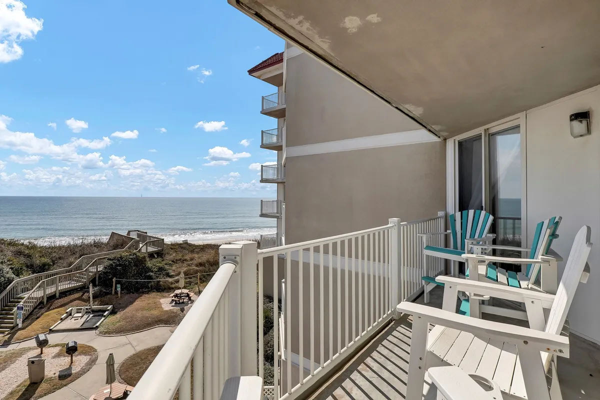 A tranquil balcony setup featuring two Adirondack chairs overlooking the expansive ocean. Soft natural light bathes the scene, and the horizon suggests endless sunrise and sunset possibilities. The setting invites quiet relaxation, morning coffee, or an intimate evening conversation, perfectly framing the coastal atmosphere.